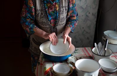 Russian grandmother washes dishes in a basin in the village