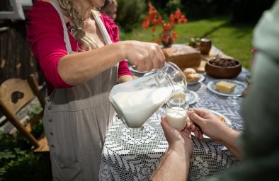 A mother pours fresh cow's milk from a jug for her son. Breakfast in the countryside.
